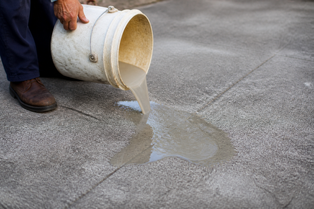 Seau de composé liquide versé sur surface béton grise