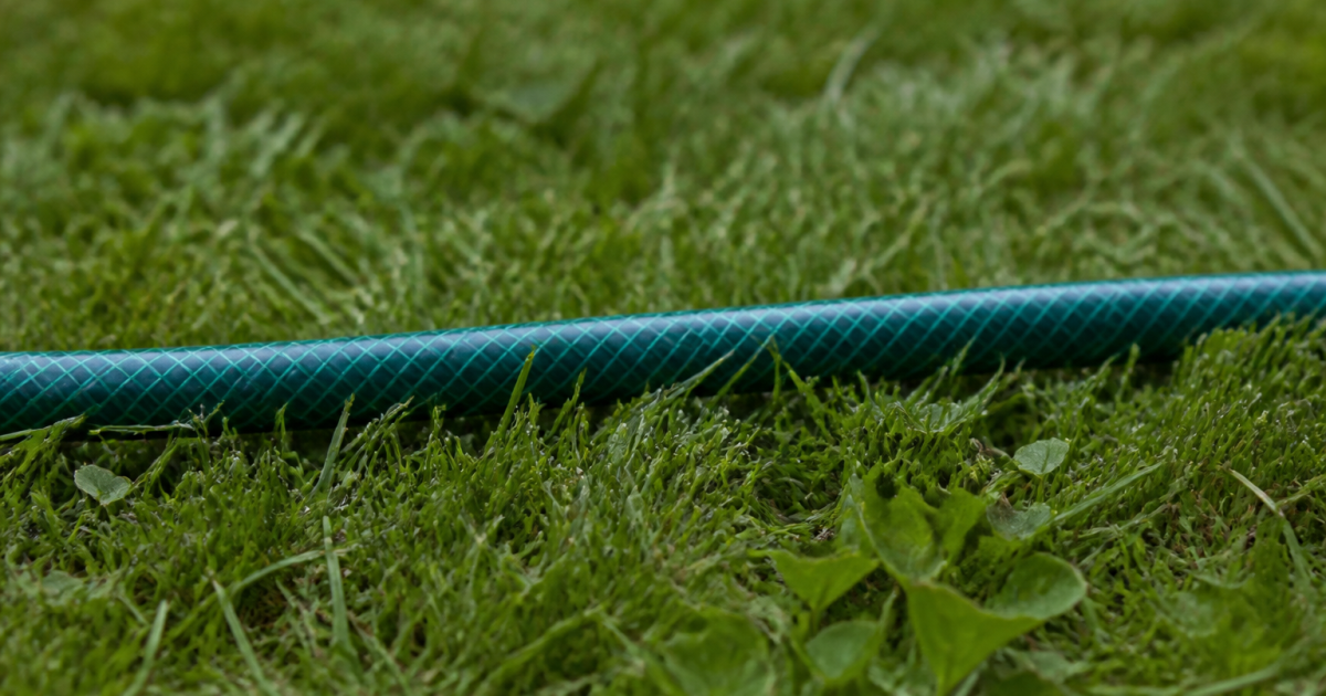 Tuyau d'arrosage posé horizontalement sur herbe verte